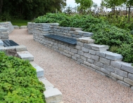 Moderner Garten- und Landschaftsbau: Gehweg und Mauern aus Natursteinen mit integrierten Sitzbänken und Anpflanzungen
